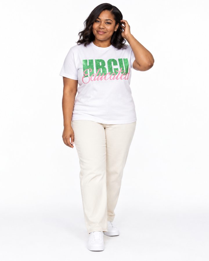 Model in a relaxed hair-touch pose wearing a white short-sleeve HBCU Educated Tee with green glitter lettering and matte pink script.
