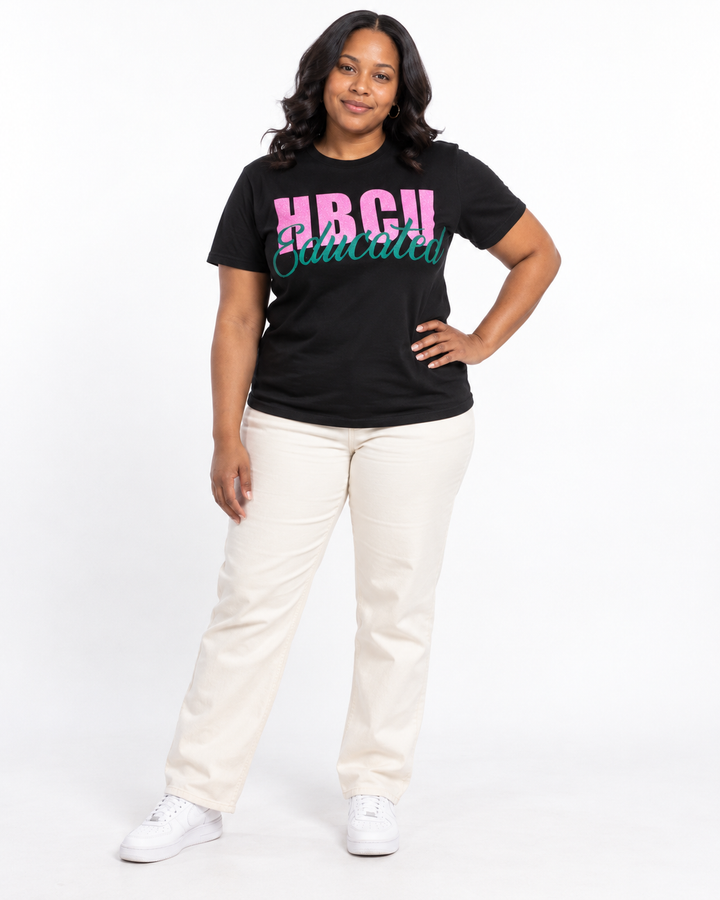 Model in a relaxed hand-on-hip pose wearing a black short-sleeve HBCU Educated Tee with pink glitter lettering and matte green script.