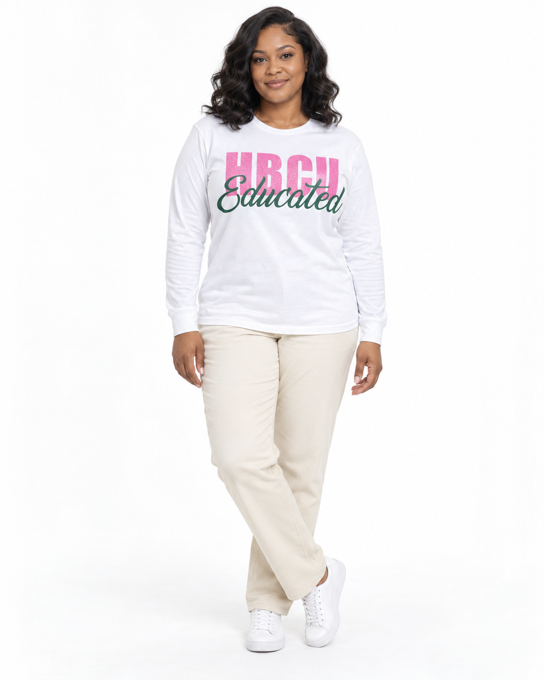 Model in a relaxed crossed-ankle pose wearing a white long-sleeve HBCU Educated Tee with pink glitter lettering and matte green script.