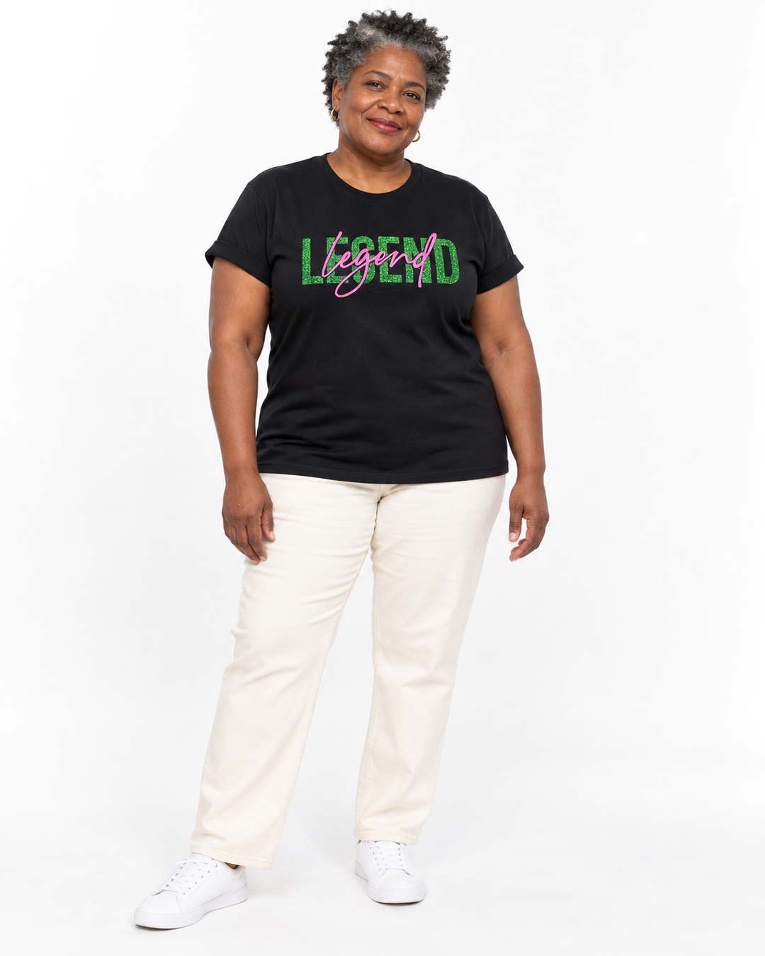 Model with short salt-and-pepper curls wearing a black short-sleeve Legend Tee with green glitter LEGEND and pink cursive legend lettering.
