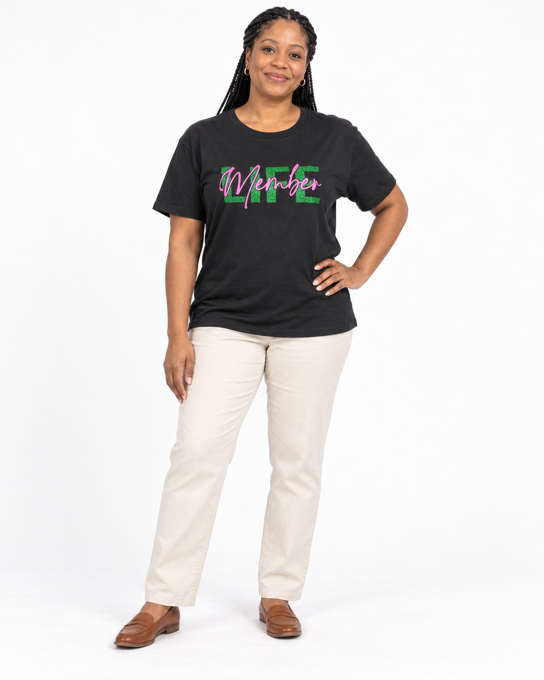 Model with braids and tan loafers wearing a black short-sleeve crew-neck Life Member Tee with green glitter LIFE and pink Member script.